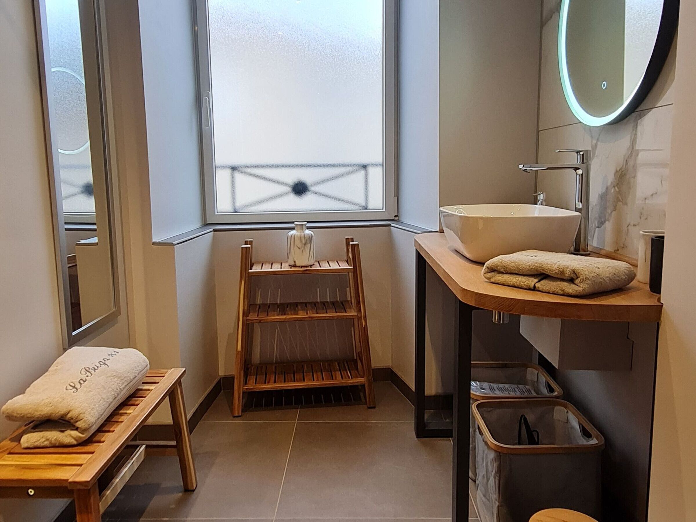 Une salle de bain moderne avec une grande fenêtre, un banc en bois, un lavabo et un miroir.