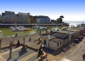 A marina with boats docked, a cyclist on a path, and buildings with balconies overlooking the water. - Crossing T2 with Balconies and Parking in Pouliguen (Le Pouliguen)