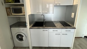 Una kitchenette compacta con lavadora integrada, microondas y pileta.