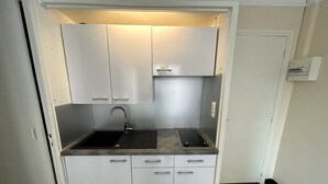 Una kitchenette compacta con pileta, grifo y encimera, que presenta gabinetes blancos y una lámpara colgante.