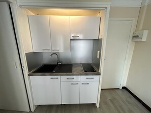 A compact kitchenette with a sink, faucet, and countertop, featuring white cabinets and a light fixture above. - Apartment for 4, balcony sea view (Argelès-sur-Mer)