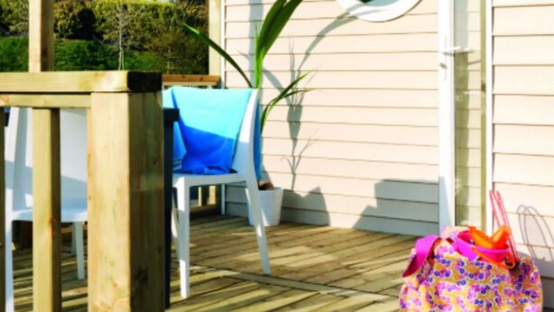 Une terrasse en bois avec une chaise blanche et un sac coloré.