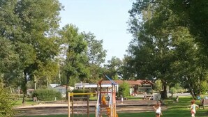 Une aire de jeux avec un toboggan et des structures d’escalade, le tout entouré d’arbres et bordé d’une pelouse.