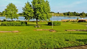 Parque con muelle de madera, césped verde, árboles y una masa de agua al fondo.