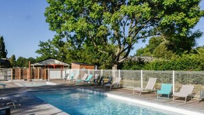Una piscina rectangular con una terraza de madera y sillas de descanso.