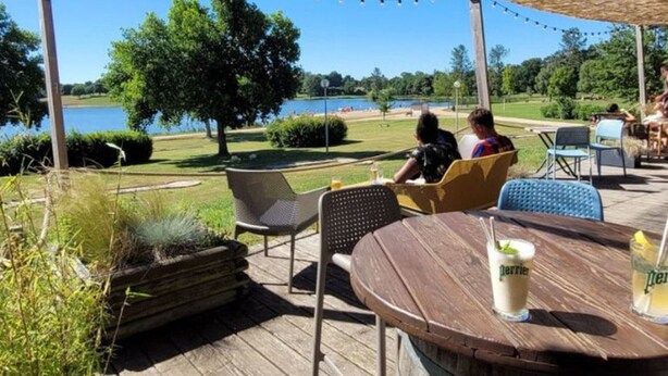 Un espacio exterior con mesas y sillas, con vista a un lago y vegetación.
