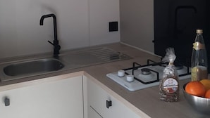 A modern kitchen with a stainless steel sink, a gas stove, and a countertop with a cutting board and a bottle of olive oil. - Cozy mobile home with terrace for 4 people (Le Pradet)