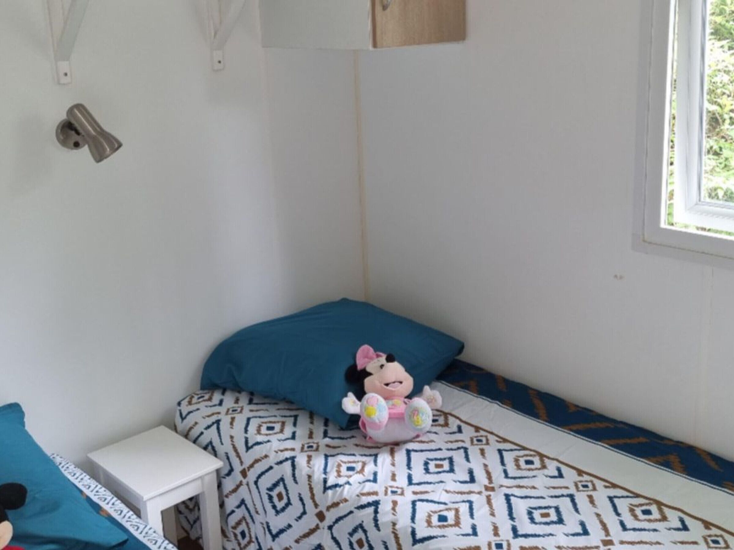 Ein Schlafzimmer mit einem Bett, einem kleinen Nachttisch, einem Fenster und einer Wandleuchte.