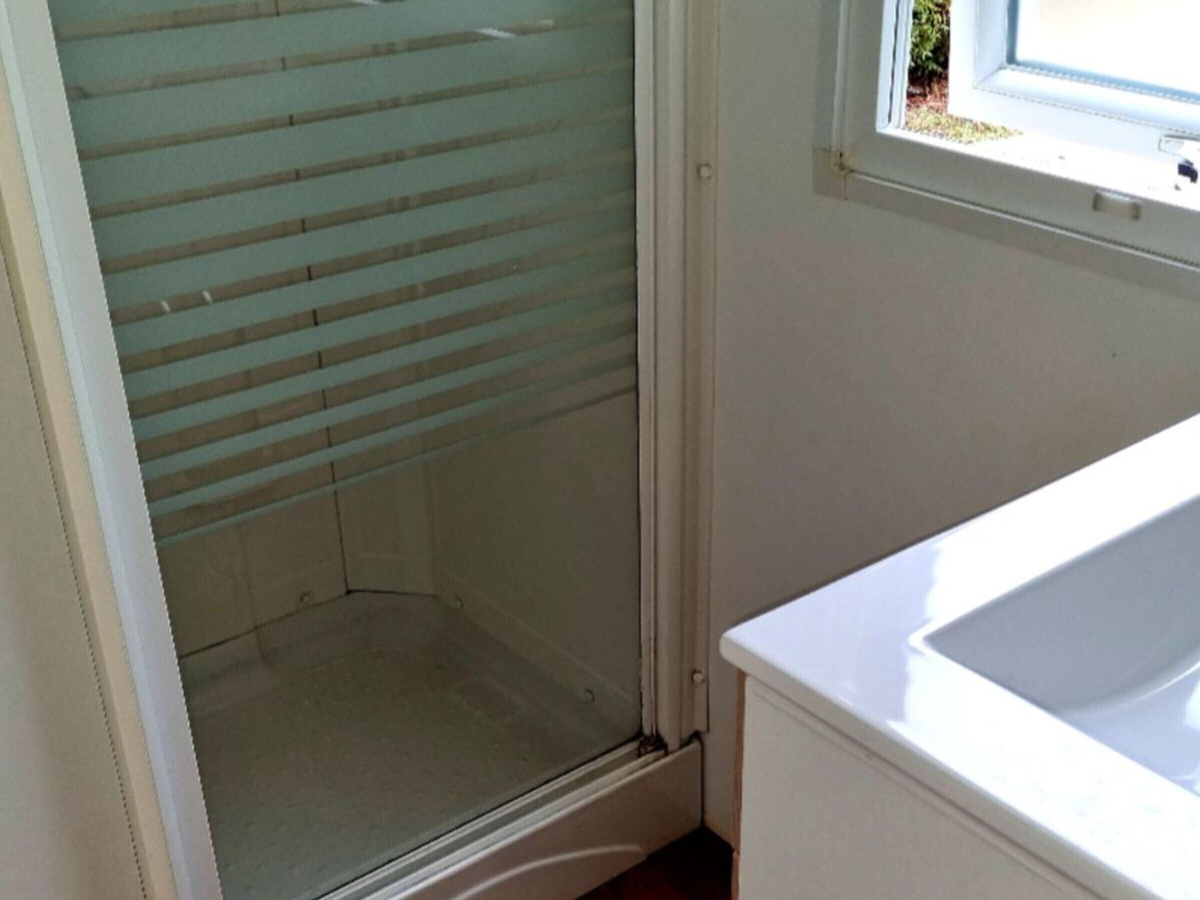 Een kamer met een glazen deur naar een douchegedeelte, een wit wastafelmeubel en een raam met uitzicht op groen buiten.