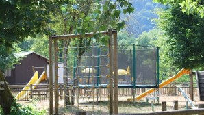 Um parquinho com uma estrutura de escalada cercada por rede, escorregadores e uma área isolada por cerca.
