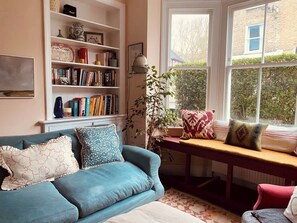 Un salon chaleureux avec un canapé bleu, une bibliothèque, une fenêtre donnant sur un beau paysage et une petite table agrémentée de coussins.