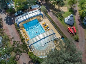 Vue aérienne d’une propriété dotée d’une piscine, de chaises longues et d’un patio couvert.