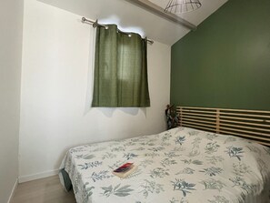 Quarto com cama, parede verde e janela com cortinas.
