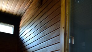 A wooden cabin interior with a bench, a small window with blinds, and a door. - Saimaa Style Spa Chalet (Imatra)