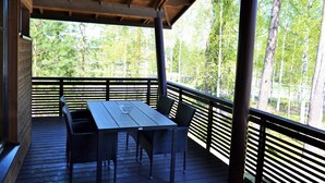A covered outdoor deck with a wooden table and chairs, surrounded by a wooden railing, overlooking a forested area. - Saimaa Style Spa Chalet (Imatra)