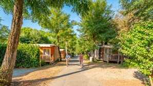 A rural road leading to a row of wooden mobile homes with a cyclist in the distance. - Mobile home with terrace, 3 bedrooms, for 6 people (Rivedoux-Plage)