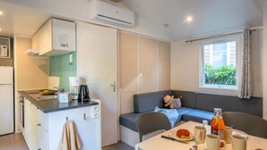 A compact kitchen with a coffee maker, a kettle, and a small dining table set with plates, cups, and a bottle. - Mobile home with terrace, 3 bedrooms, for 6 people (Rivedoux-Plage)