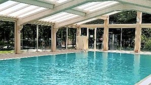 An indoor swimming pool with clear blue water, a colorful inflatable ring, and a covered area with glass walls. - Spacious chalet with terrace for 5 people (Nibelle)