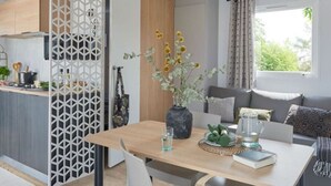 Una cocina moderna con encimera de madera, un separador decorativo blanco y un rincón comedor con una mesa para dos.