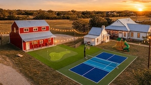 A red barn, a white house, and a tennis court with a green field and trees in the background.