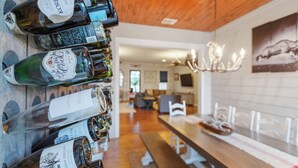 A wine cellar with bottles lined up on shelves, a wooden ceiling, and a dining area in the background.