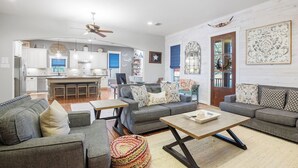 A spacious living area with a sofa set, a coffee table, and a kitchen in the background.