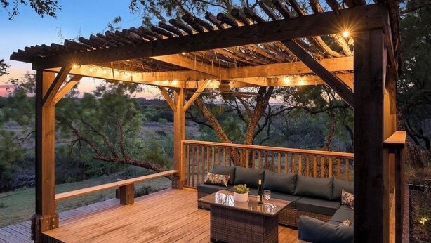 A wooden deck with a pergola, outdoor seating, and a view of the surrounding landscape.