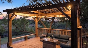 A wooden deck with a pergola, outdoor seating, and a view of the surrounding landscape.