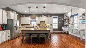 A modern kitchen with white cabinetry, a central island with stools, and pendant lighting.
