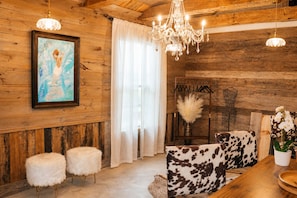 A rustic interior with wooden walls, a chandelier, a framed painting, and a cow-patterned sofa.