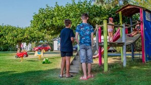 Un'area giochi con scivolo e strutture per arrampicarsi, circondata da erba e alberi.