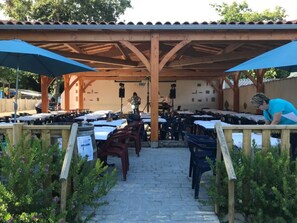 An outdoor patio with tables and chairs, covered by a wooden structure with blue umbrellas. - Functional Mobile Home in Jard-sur-Mer, 3 Bedrooms, Sleeps 6 (Jard-sur-Mer)