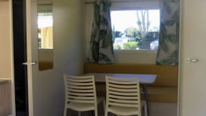 A room with two white chairs, a small table, and a window with a curtain. - Comfortable Mobile Home with Terrace in Cavaillon (Cavaillon)