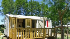 A mobile home with a wooden deck and a red door, surrounded by trees. - Comfortable Mobile Home with Terrace in Cavaillon (Cavaillon)