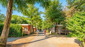 A rural road leading to a row of wooden mobile homes with a cyclist in the distance. - Mobile home 4 pers with terrace in Rivedoux-Plage (Rivedoux-Plage)