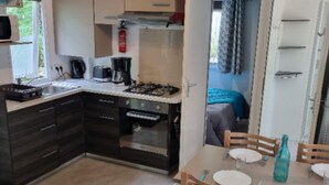 Une cuisine de taille réduite, dotée de meubles de couleur sombre, d’une cuisinière à gaz et d’un coin repas avec des chaises et une table en bois, le tout disposé pour deux personnes.