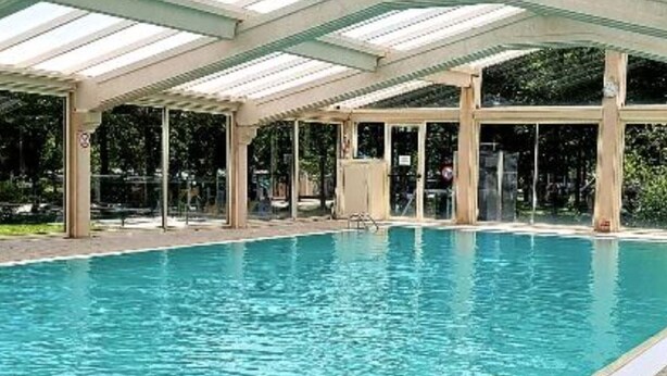En inomhuspool med kristallklart blått vatten, en färgglad uppblåsbar badring och ett avskärmat område med väggar av glas.