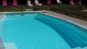 Piscina retangular com água cristalina, rodeada por um deck revestido com azulejos.