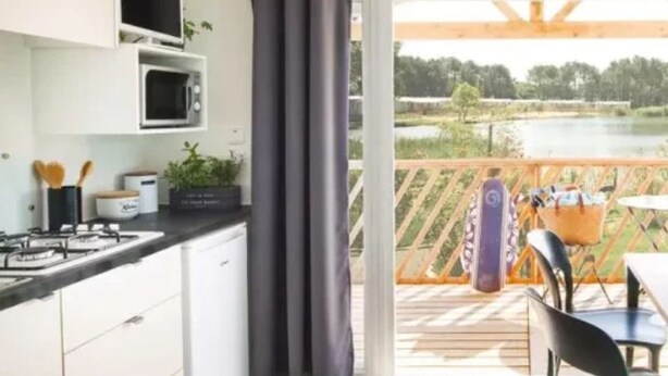 Cozinha moderna com fogão a gás, micro-ondas e armários, com acesso a uma varanda e vista para um lago, além de móveis de exterior.