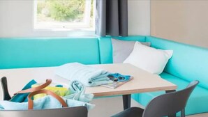 Um quarto com um sofá verde-água, uma mesinha e uma cadeira. Há uma cesta com roupas e um par de óculos de sol na mesa.