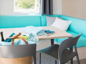A room with a teal sofa, a small table, and a chair. There is a basket with clothes and a pair of sunglasses on the table. - Mobile Home with Terrace, Sleeps 4, 2 Bedrooms (Sandrans)