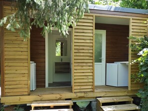Een houten blokhut met een veranda, een deur die naar een keuken leidt, en een kleine koelkast van binnen.