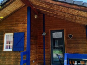 Una cabaña de madera con una puerta azul, un cartel con el número 17 y una decoración con forma de corazón en la pared.