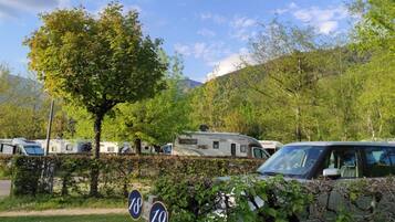 Un terrain de camping avec des camping-cars et une voiture, entouré d’arbres et de collines.