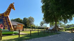 Puistossa on kirahvin patsas, pieni rakennus ja puu.
