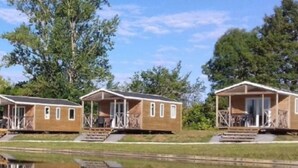 A row of wooden cabins with balconies, a small pool, and a clear reflection in the water. - Chalet for 6 with Terrace and Equipped Kitchen (Lamontjoie)