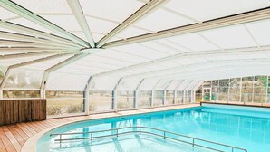 Une piscine couverte dotée d’une terrasse en bois et de murs en verre.