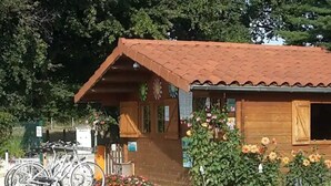 A wooden building with a tiled roof, a bicycle parked in front, and a flower bed with various flowers. - Mobile home for 2 with terrace (Sandrans)