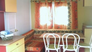 A compact kitchen with a bench seating area, a small table, and white chairs. - Mobile home 32m² with terrace, 3 bedrooms in Cavaillon, 8 pers. (Cavaillon)