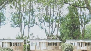 A row of two-story mobile homes with wooden decks, surrounded by lush green trees. - Mobile home 32m² with terrace, 3 bedrooms in Cavaillon, 8 pers. (Cavaillon)